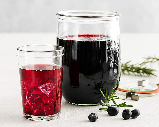 Hjemmelavet blåbærsaft i glas og kande med blåbær og rosmarin