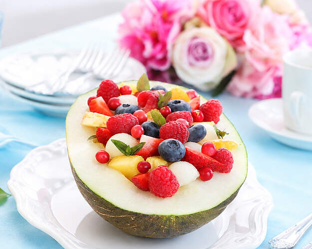 Halv Piel De Sapo melon serveret med friske bær, blåbær, hindbær og melonstykker som sommerdessert