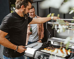 To mænd tilbereder mad på en gasgrill - guide til valg af kulgrill, gasgrill og elgrill