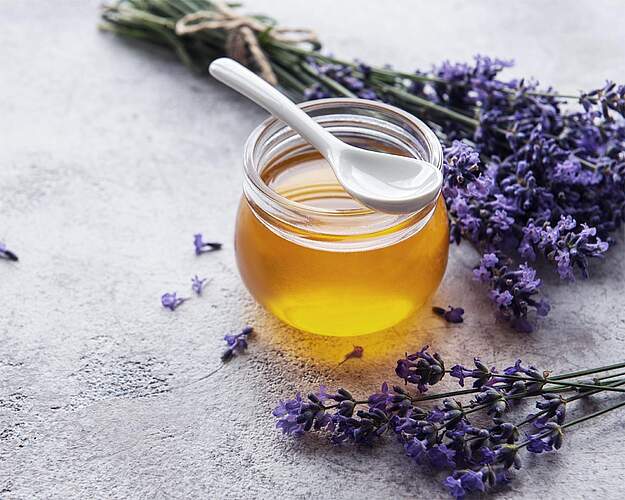Hjemmelavet lavendelhonning i glas med friske lavendelblomster ved siden af