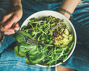 Person med skål fyldt med grøn salat, avocado og friske blade