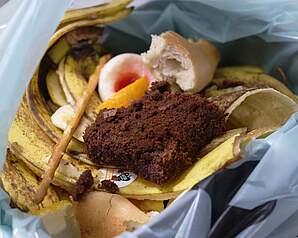 Madrester, brød og frugtskræller i skraldepose som illustration til madspild i hjemmet
