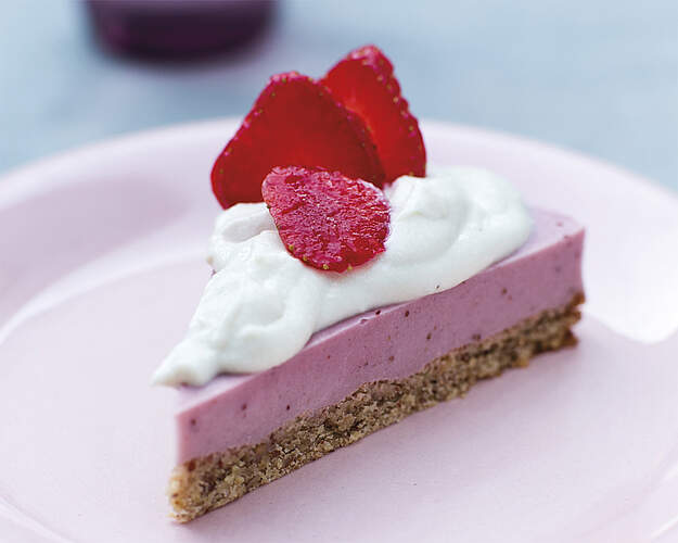 Mælkefri jordbær cheesecake med mandelbund, cremet jordbærfyld, flødeskumslignende topping og friske jordbær på tallerken
