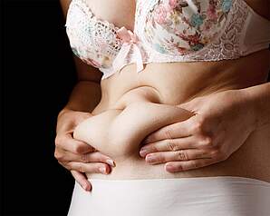 Kvinde tager fat om maven som illustration til overvægt, Wegovy, vægtbehandling og hjerte-kar-risiko