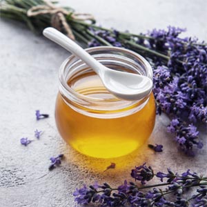 Hjemmelavet lavendelhonning i glas med lavendelblomster ved siden af